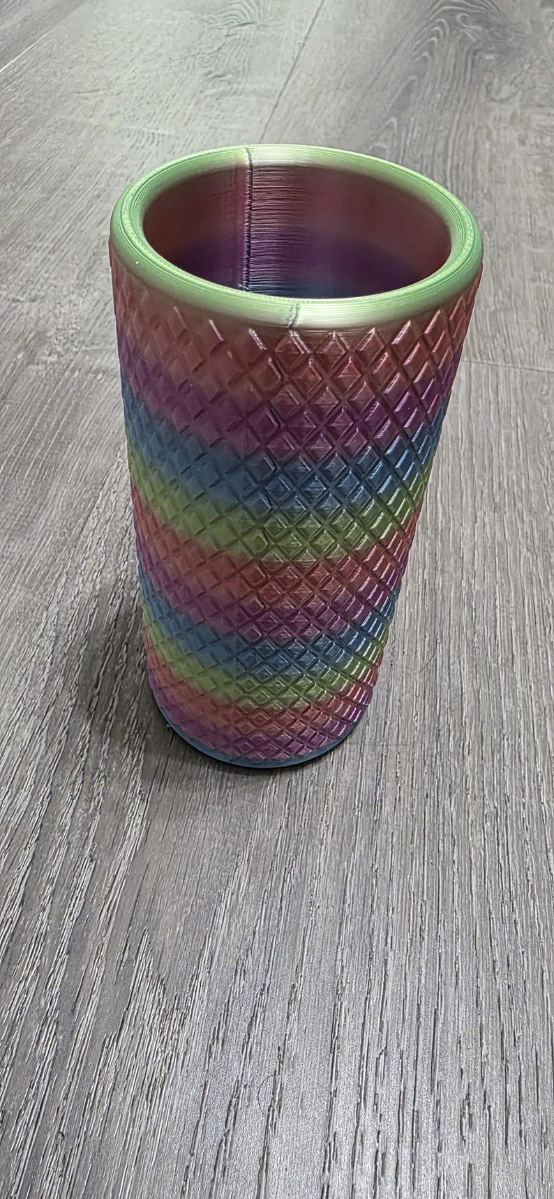Puede incluir: Un vaso cil&iacute;ndrico con un acabado degradado de arco&iacute;ris vibrante que transita por tonos verdes, azules, morados y rosas. La superficie exterior est&aacute; cubierta con una textura de rejilla en forma de diamante en relieve.