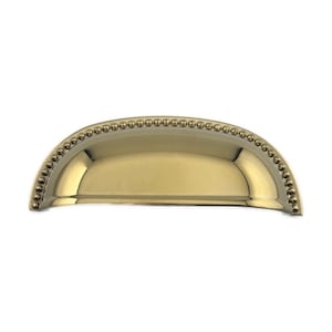 May include: A gold-colored, half-moon shaped cabinet pull. The pull has a smooth, curved interior and is bordered by a row of small, round decorative beads. The hardware is designed for easy installation and adds a touch of elegance to any furniture piece.