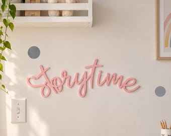 Puede incluir: Un letrero de pared en color rosa con la palabra "storytime" en letra cursiva, acompañado de calcomanías circulares grises y rosas. La escena incluye un estante blanco con un conejo de peluche y una cesta tejida con un cojín de corazón.