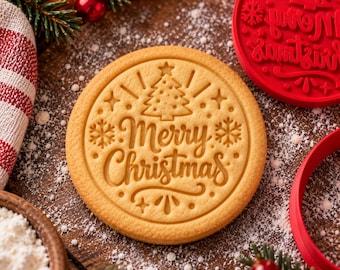Puede incluir: Una galleta redonda de color tostado claro con el texto Merry Christmas, un árbol de Navidad central y copos de nieve. La galleta está sobre una superficie de madera oscura espolvoreada con harina blanca, junto a un cortador circular rojo.
