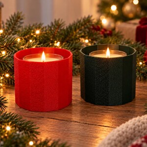 May include: Two cylindrical candles in faceted holders, one bright red and one dark green, each containing a lit candle with a visible flame. The holders have a textured, matte finish and a vertical ribbed design, housing clear glass candle inserts.