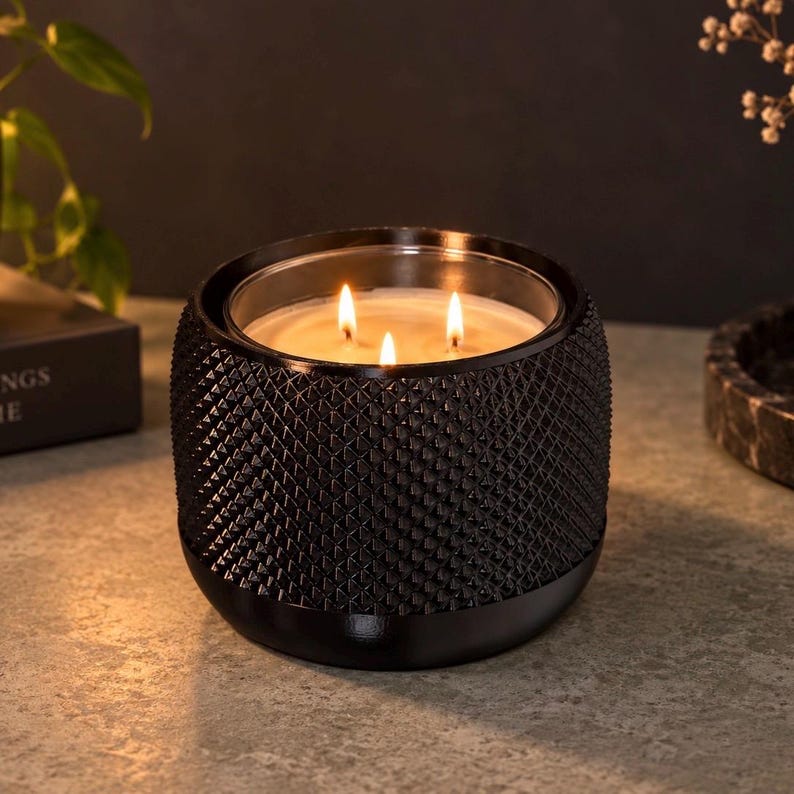 Black candle holder with a dotted pebble texture holding a lit 3-wick candle