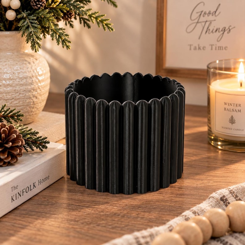 May include: A matte black cylindrical planter featuring a vertical fluted or ribbed texture along the exterior. The container has a scalloped top edge and a hollow interior, designed with a consistent, repeating pattern of rounded vertical columns.