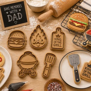 May include: A collection of brown plastic cookie cutters shaped like a burger, flames with the word DAD, a cutting board with the text KING OF THE GRILL, a grill, and a spatula, alongside decorated cookies and a sign reading BAKE MEMORIES WITH DAD.