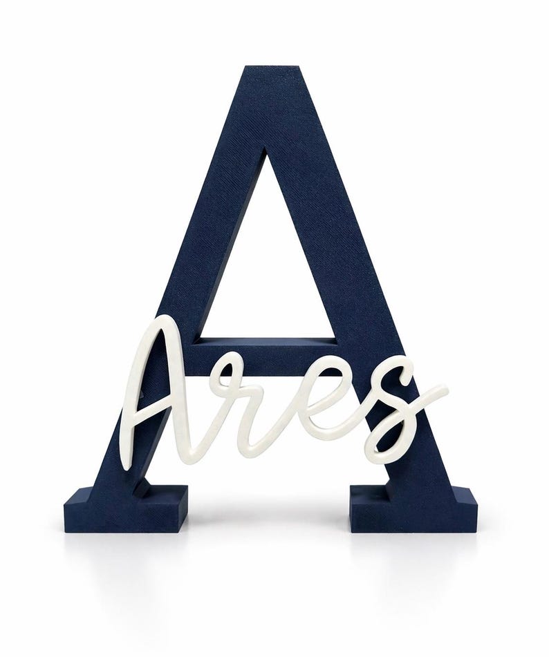 May include: A navy blue wooden letter "A" with the name "Ares" in white script. The letter is freestanding and has a textured surface. The name is in a cursive font.