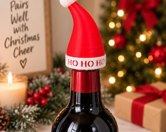 Puede incluir: Un tapón para botella con forma de gorro de Papá Noel rojo y blanco, con un pompón blanco en la punta y una banda blanca en la base con el texto HO HO HO impreso en rojo. El gorro está colocado sobre el cuello de una botella de vidrio oscuro.
