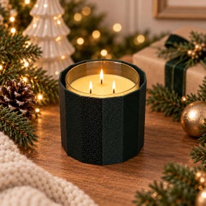 Puede incluir: Una vela de tres mechas en un recipiente cil&iacute;ndrico de color verde oscuro, facetado y texturizado. La cera es de color crema p&aacute;lido y las tres mechas est&aacute;n encendidas, produciendo llamas peque&ntilde;as y brillantes. El recipiente tiene una forma geom&eacute;trica.