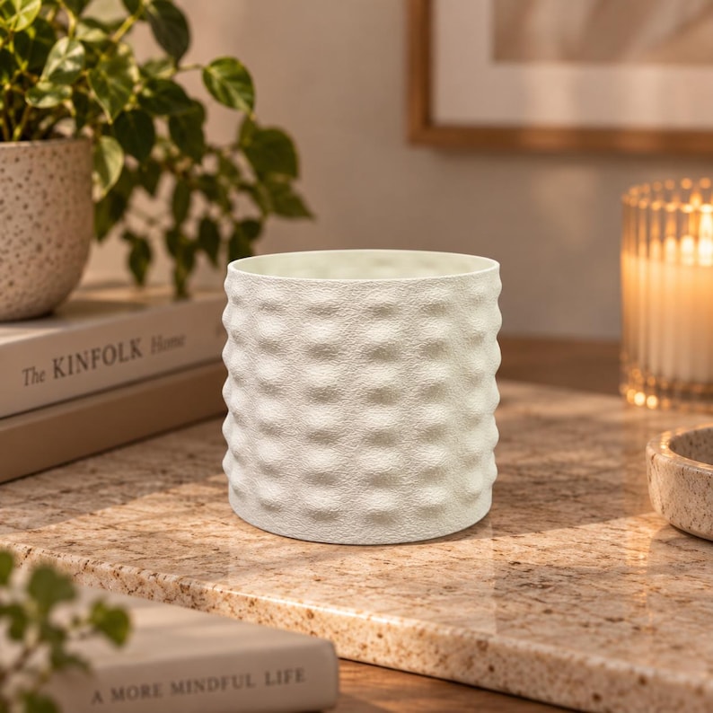 May include: A cylindrical off-white planter featuring a repeating dimpled, textured surface pattern. The vessel has a straight rim and a uniform, matte finish, designed with a consistent grid of rounded indentations across its entire exterior.