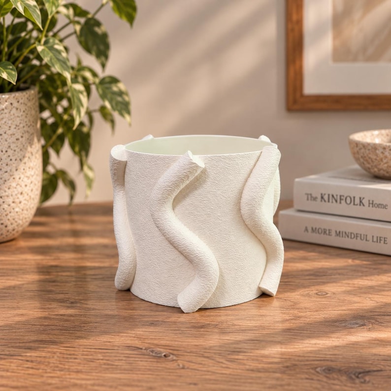 May include: A cylindrical off-white planter featuring a textured surface and three prominent, raised, vertical wavy accents that wrap around the exterior. The vessel has a wide, open top and a smooth interior finish, designed for holding small plants.