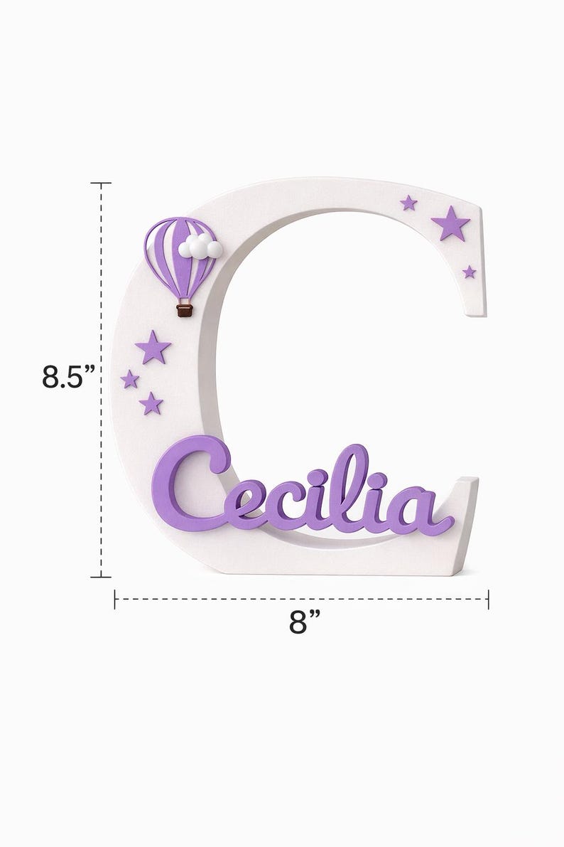 Może przedstawiać: Biała drewniana litera "C" z imieniem "Cecilia" w fioletowym skrypcie. Litera ma 21,6 cm wysokości i 20,3 cm szerokości. Zawiera fioletowy balon na ogrzane powietrze, chmury i gwiazdy. Element dekoracyjny do pokoju dziecięcego.