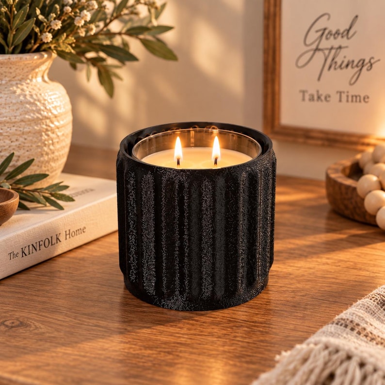 Black ribbed column candle holder with a lit candle on a wooden shelf next to books