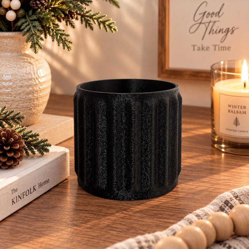 May include: A cylindrical black planter with a textured, vertically ribbed exterior surface. The container features a matte finish and a wide, open top, designed with a consistent pattern of deep grooves running from the top rim to the base.