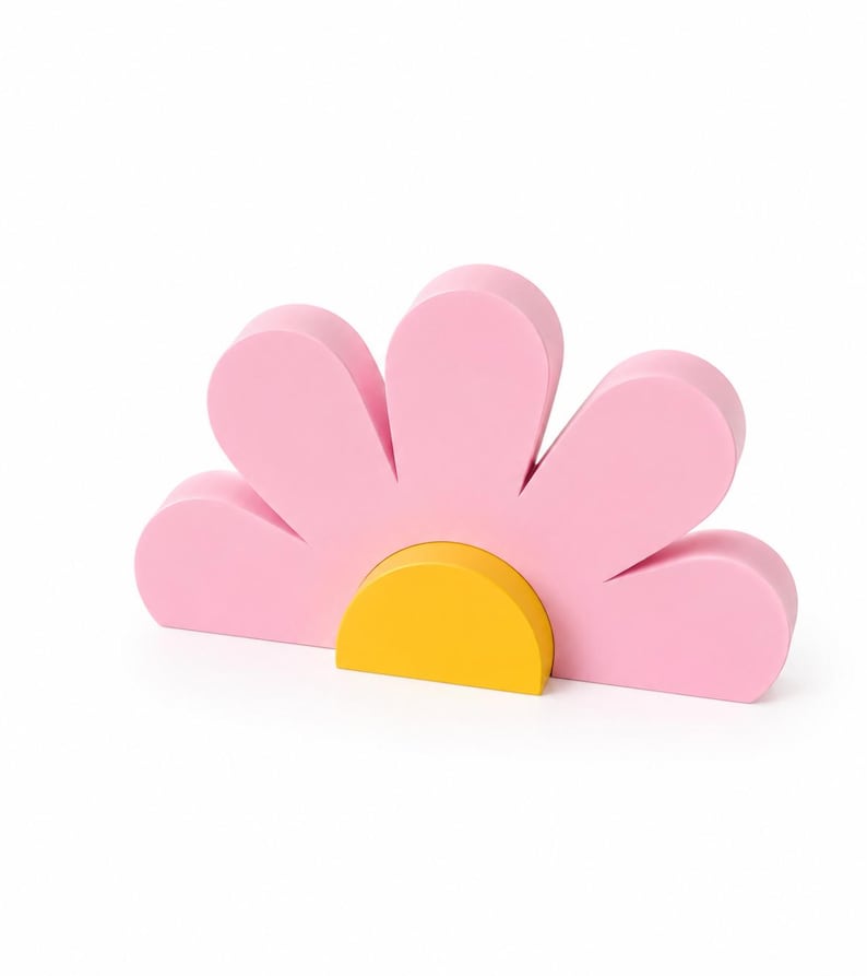 K&ouml;nnte beinhalten: Ein rosa bl&uuml;tenf&ouml;rmiges Dekorationsobjekt mit gelber Mitte. Die Blume hat sechs abgerundete Bl&uuml;tenbl&auml;tter und besteht aus einem festen Material. Das Design ist schlicht und modern, geeignet f&uuml;r die Inneneinrichtung.