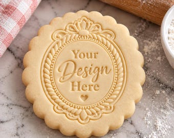 May include: A round, scalloped-edge cookie dough stamp featuring an ornate, rope-style circular frame with a decorative crest at the top. The center is embossed with the text Your Design Here and a small heart icon at the bottom.