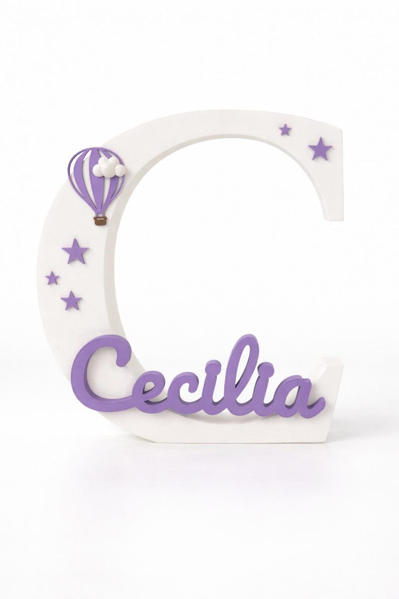 May include: A white wooden letter "C" with the name "Cecilia" in purple script. The letter is decorated with purple stars and a purple hot air balloon with a white cloud.