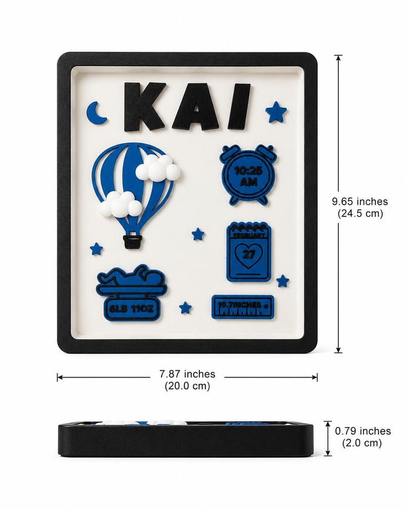 May include: A rectangular black-framed wall sign with a white background featuring the name KAI in black letters. It includes blue icons of a hot air balloon, an alarm clock showing 10:25 AM, a calendar showing February 27, a baby on a scale reading 6LB 11OZ, and a ruler reading 19.7INCHES. Dimensions are 9.65 by 7.87 by 0.79 inches.