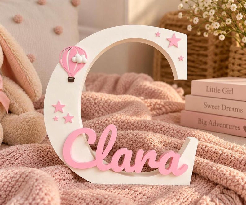 White letter C with the name Clara in pink script, a hot air balloon and clouds