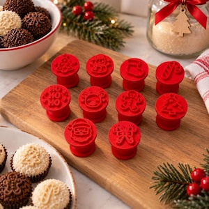 May include: A set of ten red circular cookie stamps featuring various holiday designs including a Christmas tree, snowman, stocking, candy cane, Santa Claus, gingerbread man, reindeer, and the text HO HO HO, arranged on a wooden cutting board.