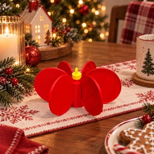 May include: A bright red, circular, multi-panel folding trivet featuring a central yellow silicone loop for hanging. The object consists of several connected, flat, round discs that expand outward from a central cylindrical core to form a star shape.