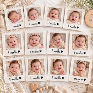 May include: A set of twelve white square photo frames arranged in a grid, each containing a photograph of a baby at different ages from 1 month to one year. Each frame is labeled with the corresponding age and a black heart icon printed below.
