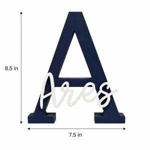 May include: A navy blue wooden letter "A" with the name "Ares" in white script. The letter is 21.6 cm tall and 19.1 cm wide. This decorative piece is suitable for nursery decor or personalized gifts.