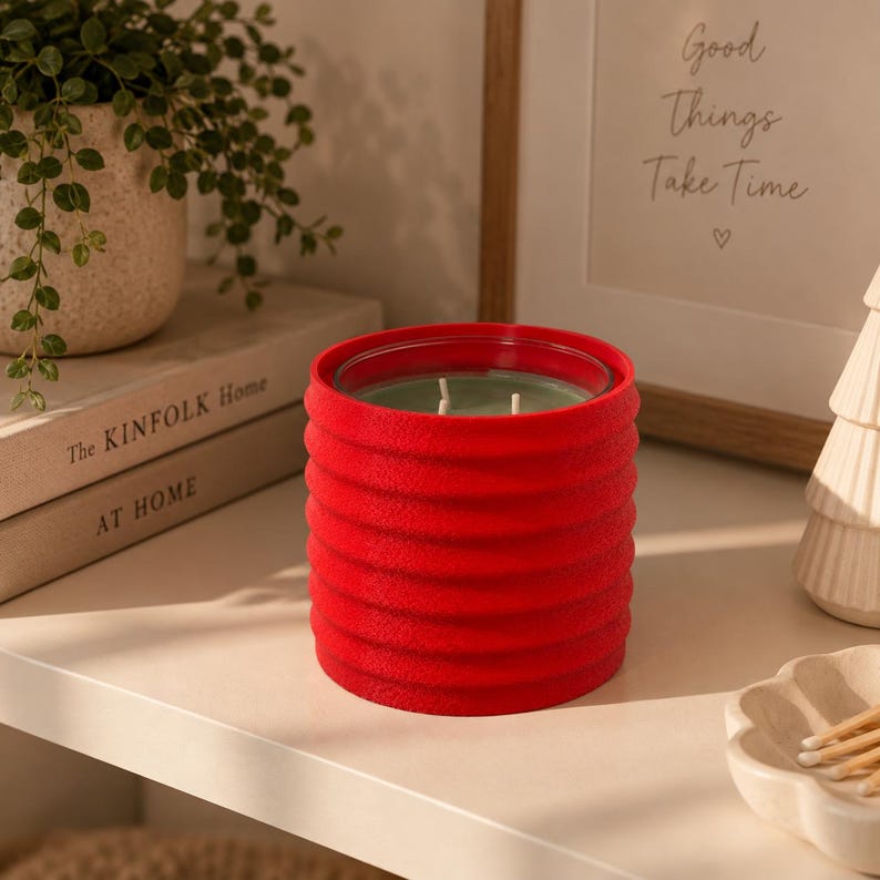 Puede incluir: Una vela cil&iacute;ndrica en un recipiente de color rojo brillante, texturizado y acanalado. La vela presenta una superficie de cera verde claro con tres mechas visibles. El exterior del recipiente tiene un acabado mate y t&aacute;ctil con crestas horizontales.