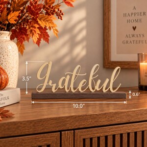 May include: A wooden tabletop sign featuring the word Grateful in a cursive script font, mounted on a dark rectangular base. The sign measures 3.5 inches in height, 10.0 inches in length, and the base has a thickness of 0.6 inches.
