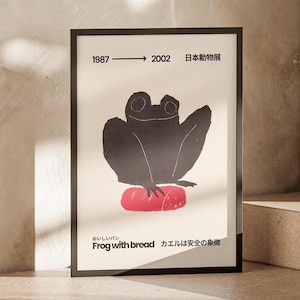 May include: Black framed art print featuring a stylized black frog sitting on a red loaf of bread. The print includes the text "Frog with bread" and Japanese text. The print also has the years 1987 to 2002.