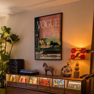 Puede incluir: Interior de una habitaci&oacute;n con un mueble de madera que exhibe discos de vinilo, un tocadiscos y una impresi&oacute;n enmarcada de "Vogue". Tambi&eacute;n se ven una estatua de caballo dorada y una l&aacute;mpara estampada. Una gran planta verde a&ntilde;ade un elemento natural.