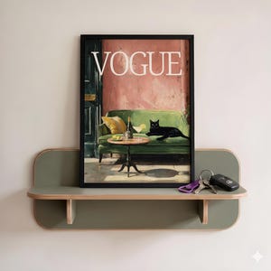 Puede incluir: Una impresi&oacute;n art&iacute;stica enmarcada "VOGUE" con una pintura de un gato negro en un sof&aacute; verde con una mesa y bebidas. La impresi&oacute;n se muestra en un estante verde y de madera, con llaves. La pared est&aacute; pintada de color claro.
