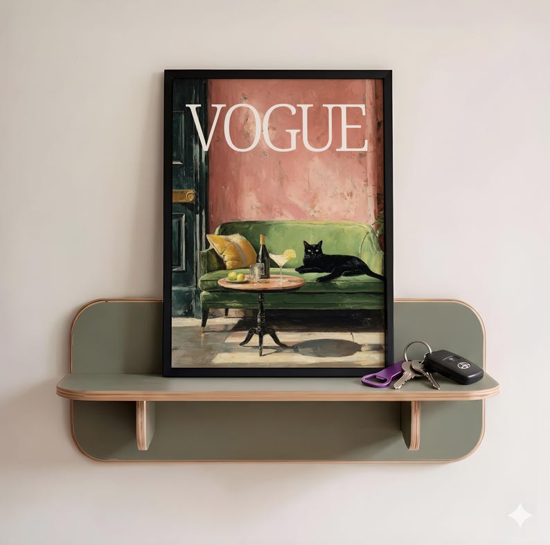 Puede incluir: Una impresi&oacute;n art&iacute;stica enmarcada "VOGUE" con una pintura de un gato negro en un sof&aacute; verde con una mesa y bebidas. La impresi&oacute;n se muestra en un estante verde y de madera, con llaves. La pared est&aacute; pintada de color claro.
