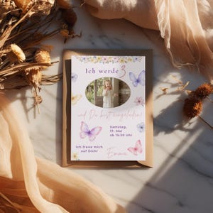 May include: A rectangular birthday invitation card featuring watercolor butterflies and flowers, with a central oval photo of a child. The text reads: Ich werde 3, und Du bist eingeladen!, Samstag, 17. Mai ab 15:30 Uhr, Ich freue mich auf Dich!, and Emma.