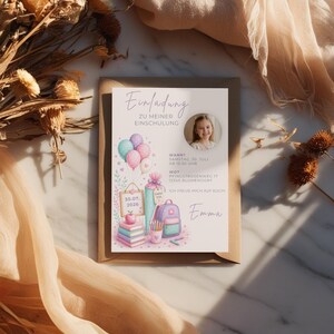 May include: A rectangular invitation card titled Einladung zu meiner Einschulung featuring a circular photo of a child, pastel-coloured balloons, a stack of books, a school cone, a backpack, and a pencil holder with the name Emma printed in script.