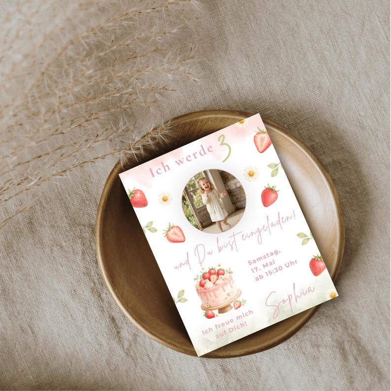 May include: A rectangular invitation card featuring a central circular photo of a child, decorated with watercolor strawberries, daisies, and a cake illustration. The text reads Ich werde 3 und Du bist eingeladen, Samstag, 17. Mai ab 15:30 Uhr, Sophia, Ich freue mich auf Dich.