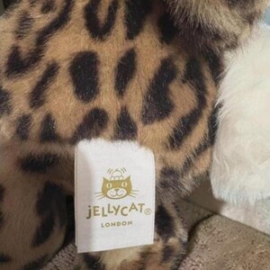 May include: A soft toy featuring a leopard print design in brown and black. A white label with the "JELLYCAT LONDON" logo is attached to the toy.