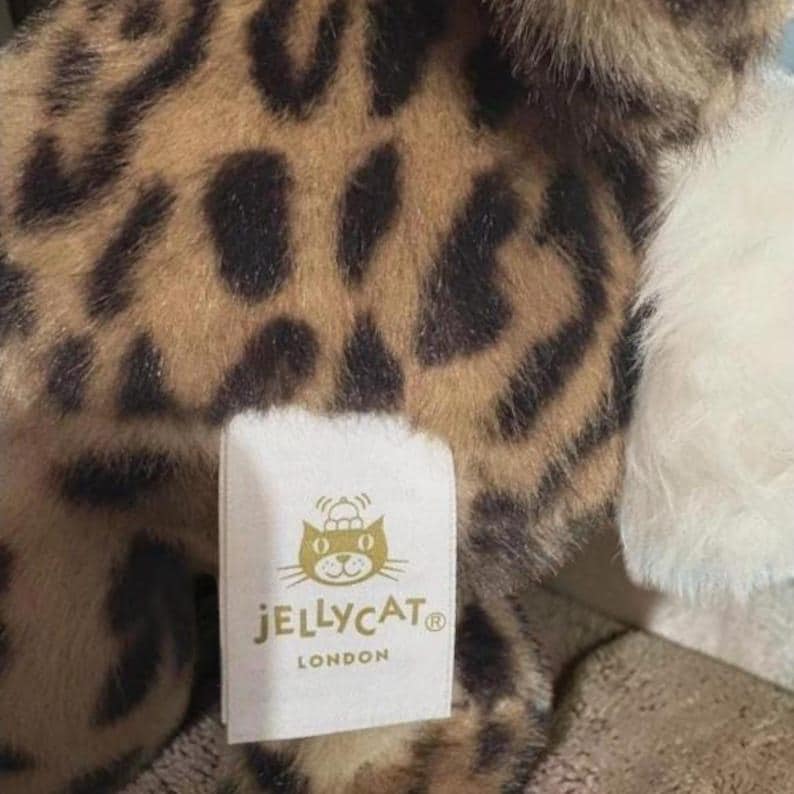May include: A soft toy featuring a leopard print design in brown and black. A white label with the "JELLYCAT LONDON" logo is attached to the toy.