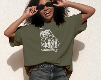 Op de afbeelding: Een olijfgroen T-shirt met korte mouwen en een witte afbeelding van de staat Georgia. Het ontwerp bevat een perzik, een boom, een rivier en een biohazard-symbool met de tekst "SAY NO TO DATA CENTERS" in het midden van de omtrek van de staat.