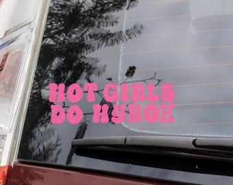 Op de afbeelding: Een roze vinyl sticker op een autoruit. De sticker leest "HOT GIRLS DO HYROX" in een bubbellettertype. De achterruit van de auto heeft een ruitenwisser en reflecteert een boom.
