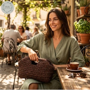 May include: A woman at a cafe table holds a brown woven handbag. She wears a green dress and smiles. A cup of coffee and sunglasses are on the wooden table. The bag has a distinctive handle. The image includes the text "YKSI CROCHETING".