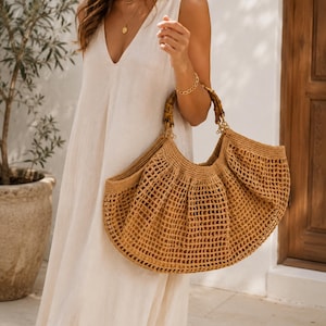 May include: A large, tan, crocheted tote bag with a wide, open-weave mesh body and two rounded bamboo handles. The bag features a crescent-shaped silhouette with a solid, tightly woven top border and a spacious, flexible structure for carrying items.