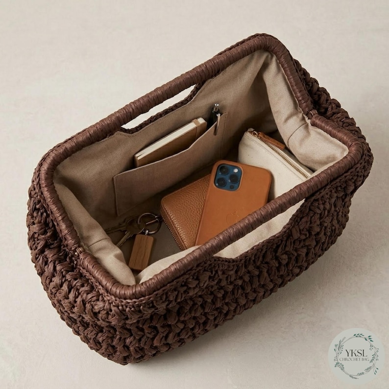 May include: A dark brown woven handbag with a rectangular shape, featuring a structured interior with pockets. Inside, a brown leather wallet, a smartphone, a small notebook, and a keychain are visible. The bag has a handle and a light-coloured interior lining.