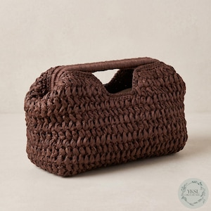 May include: A brown woven handbag with a rectangular form and a handle. The bag is made of a textured material, and the handle is a solid, rounded shape. The bag has a unique, stylish design.