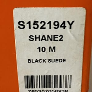 May include: A white label with black text against an orange background. The label reads "S152194Y SHANE2 10 M BLACK SUEDE" and includes a barcode and the number "765207056938".
