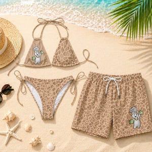 May include: A tan bikini and swim shorts set with a giraffe pattern, set on a sandy beach. The bikini top and swim shorts feature a cartoon character holding money. A straw hat, sunglasses, and seashells are also visible.