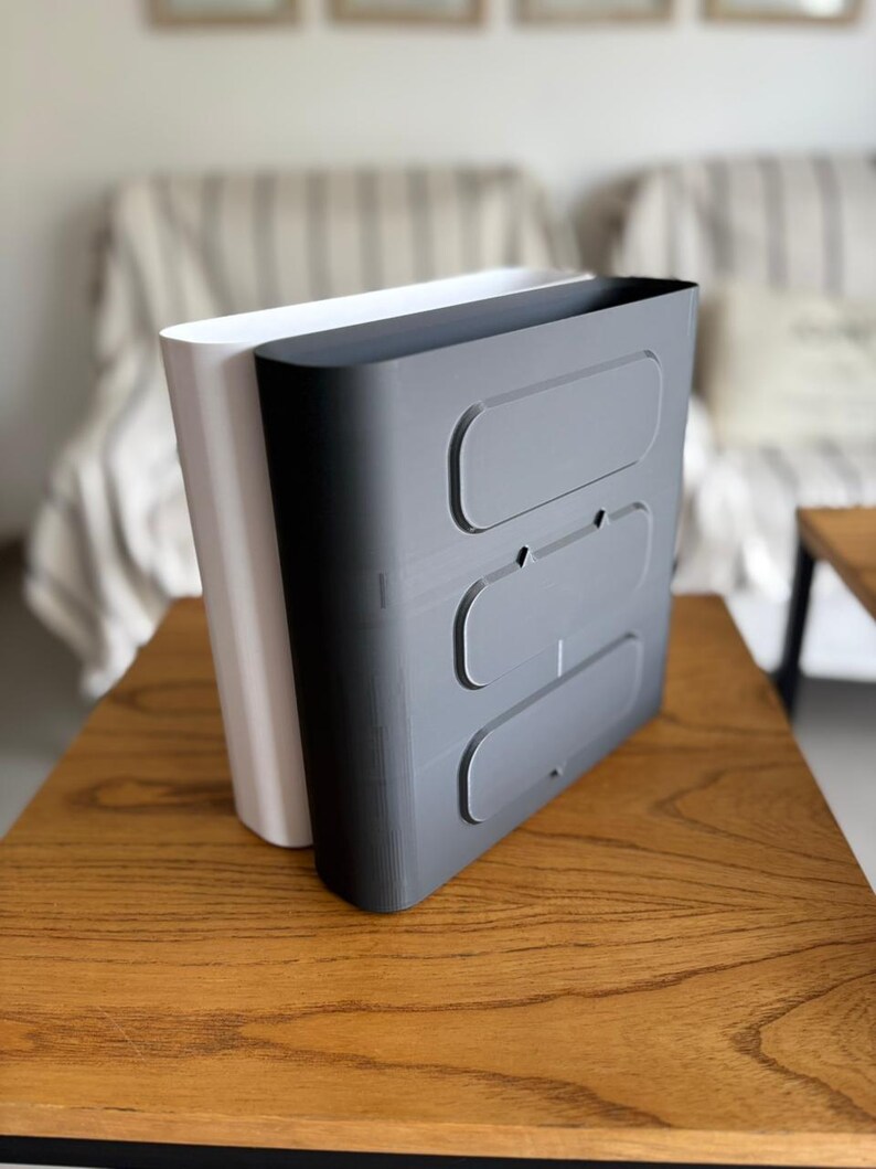 May include: A white and a dark gray vertical storage organizer with rounded edges. The dark gray unit features three horizontal, recessed oval panels on its front face, while the white unit is positioned directly behind it.