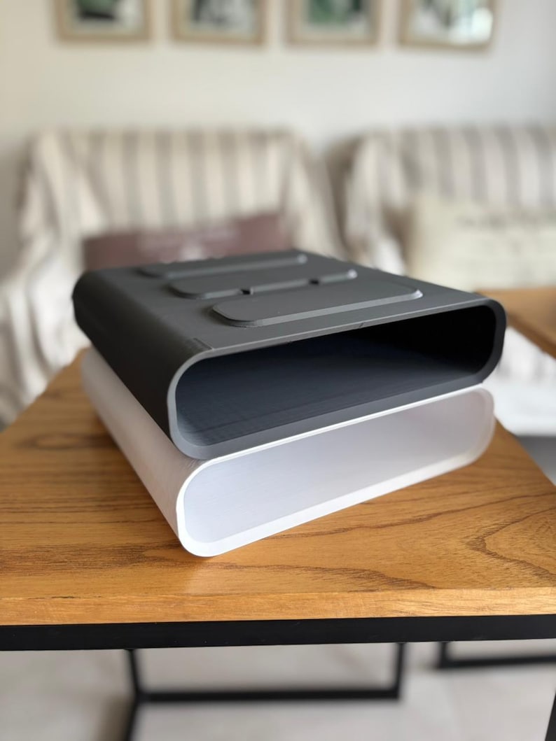 May include: A stack of two rectangular storage organizers with rounded corners. The top organizer is dark gray with three recessed rectangular indentations on the top surface, while the bottom organizer is a solid, smooth, translucent white.