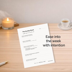 May include: A lit candle, a cup of coffee, and a journal titled "The Sunday Reset" on a wooden surface. The journal prompts reflection with the text "Ease into the week with intention."