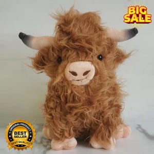 Puede incluir: Un peluche de vaca de las Tierras Altas con pelaje marr&oacute;n y lanudo, ojos negros peque&ntilde;os y nariz y pies de color rosa claro. Los cuernos son curvos con puntas negras. Se ve un texto "BIG SALE" y una insignia de "BEST SELLER".
