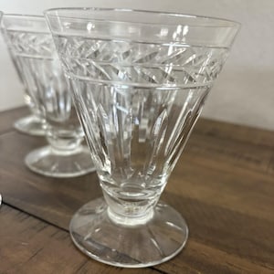 May include: Clear, vintage-style drinking glasses with a diamond-cut pattern around the rim and vertical cuts down the sides. The glasses have a flared shape and sit on a round base. The glassware is likely for serving beverages.