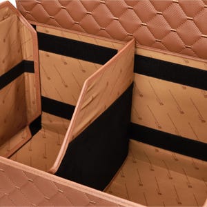May include: A tan, multi-compartment car organizer with a quilted exterior. The interior features multiple sections with black velcro straps for securing items. The organizer is designed to keep a car's interior tidy and organized.